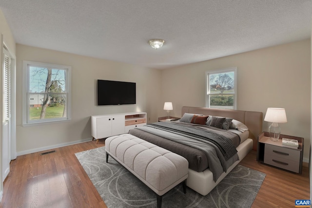 bedroom featuring a textured ceiling, light hardwood / wood-style flooring, and multiple windows