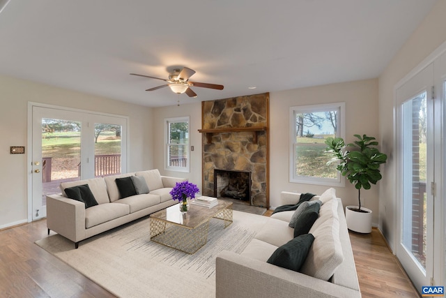 living room with a stone fireplace, light wood-type flooring, and ceiling fan