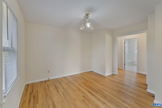 unfurnished room with a wealth of natural light, a chandelier, and light wood-type flooring