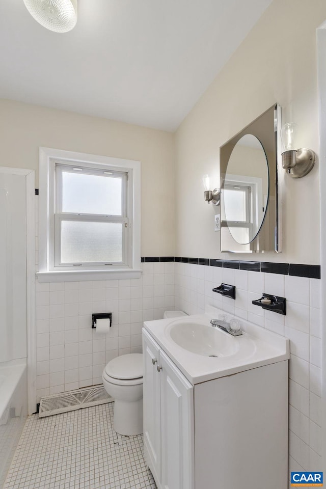 bathroom with toilet, vanity, tile walls, and tile patterned floors