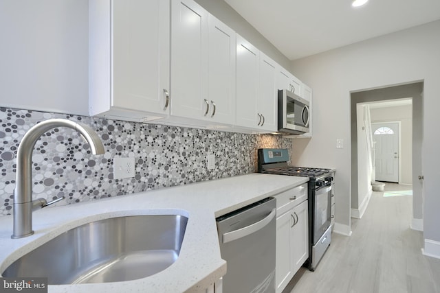 kitchen with white cabinets, sink, light hardwood / wood-style flooring, light stone countertops, and appliances with stainless steel finishes