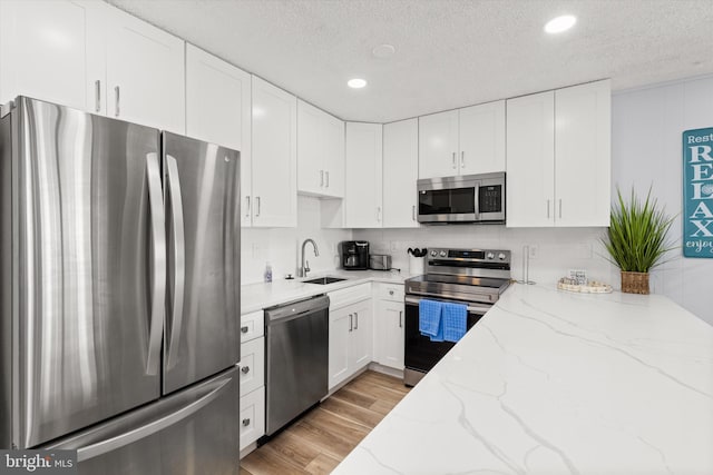 kitchen featuring stainless steel appliances, white cabinetry, a textured ceiling, light stone countertops, and sink