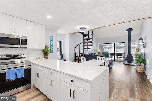 kitchen with kitchen peninsula, light hardwood / wood-style floors, white cabinetry, and appliances with stainless steel finishes