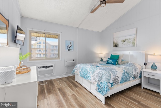 bedroom with ceiling fan, a wall mounted AC, lofted ceiling, and light hardwood / wood-style floors