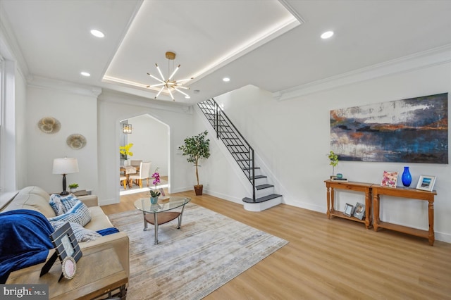 living room with crown molding, wood-type flooring, a raised ceiling, and a notable chandelier