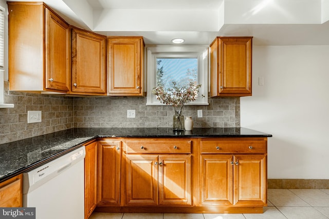 kitchen featuring white dishwasher, dark stone counters, light tile patterned floors, and backsplash