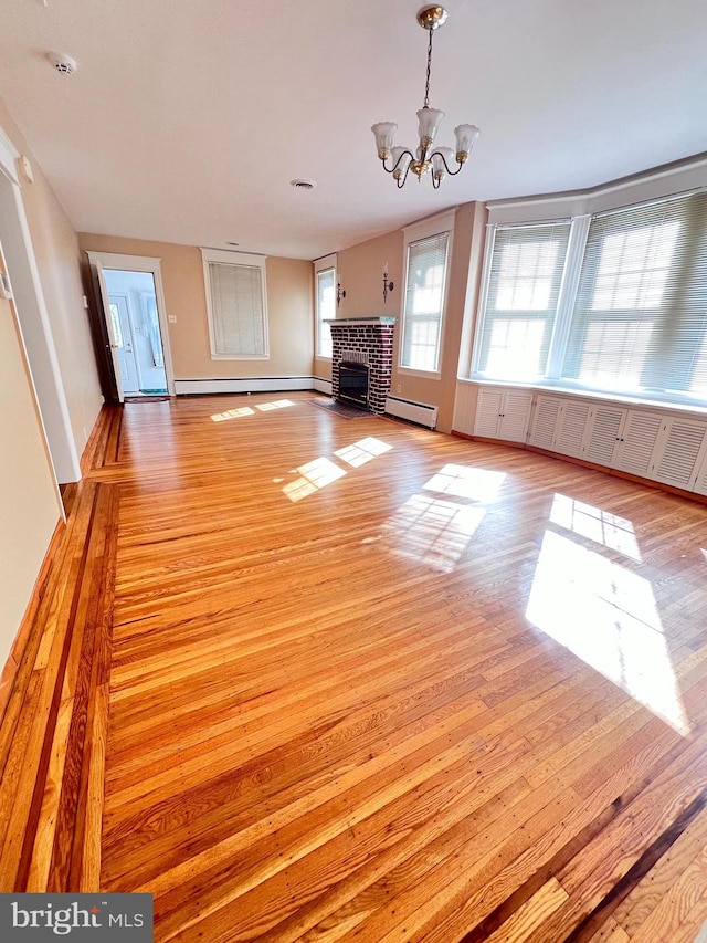 unfurnished living room with light wood-type flooring, a baseboard heating unit, and a notable chandelier