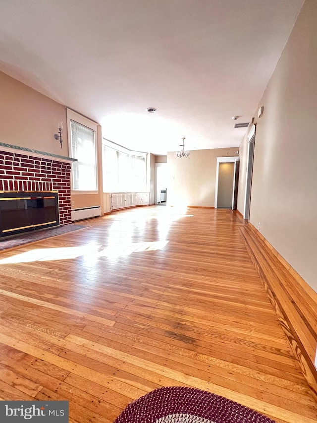 unfurnished living room with a baseboard heating unit, a brick fireplace, and light hardwood / wood-style flooring