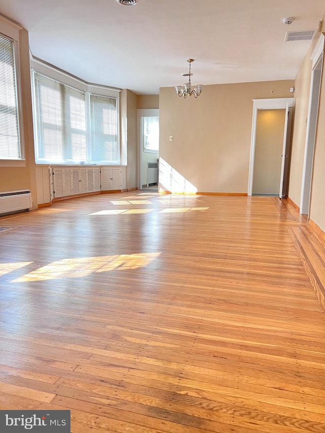 unfurnished room with a chandelier, a healthy amount of sunlight, radiator heating unit, and light wood-type flooring