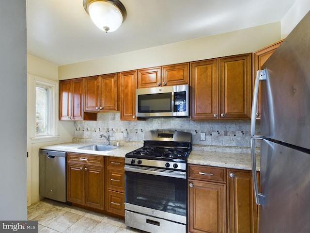 kitchen featuring appliances with stainless steel finishes, a sink, backsplash, and brown cabinets