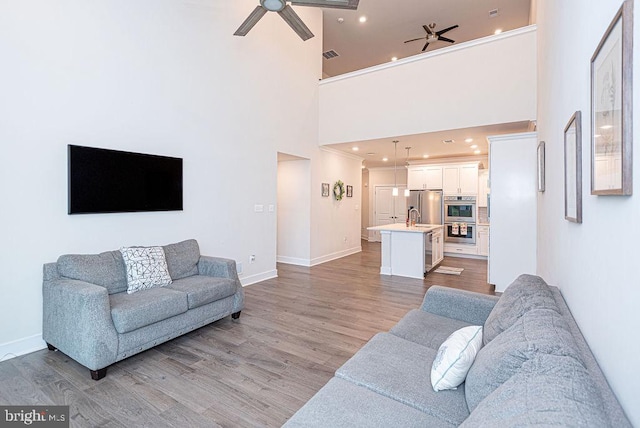 living room featuring ceiling fan, light wood-type flooring, sink, and high vaulted ceiling