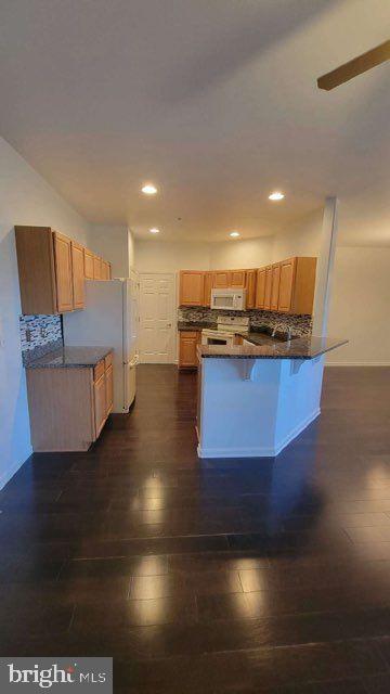 kitchen with kitchen peninsula, a kitchen breakfast bar, decorative backsplash, and dark hardwood / wood-style flooring