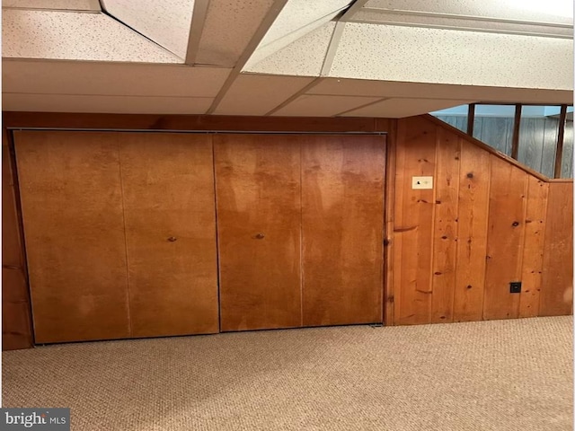 basement featuring wood walls, a drop ceiling, and carpet