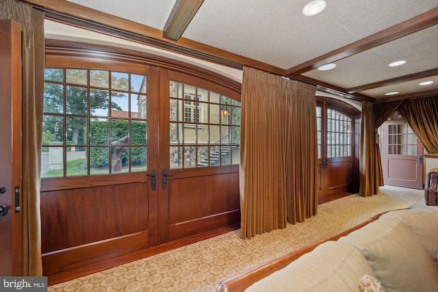 entryway featuring wood walls, beamed ceiling, carpet floors, and a textured ceiling