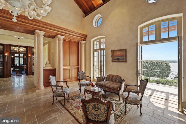 living area with a water view, a towering ceiling, a notable chandelier, decorative columns, and wooden ceiling