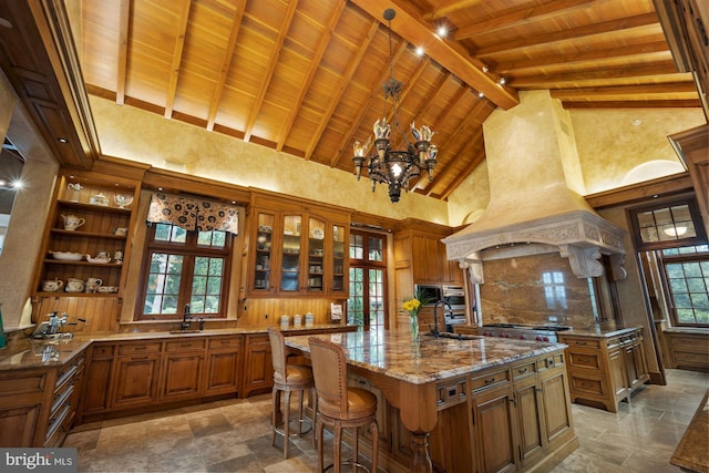 kitchen featuring beamed ceiling, a center island with sink, custom exhaust hood, high vaulted ceiling, and decorative light fixtures