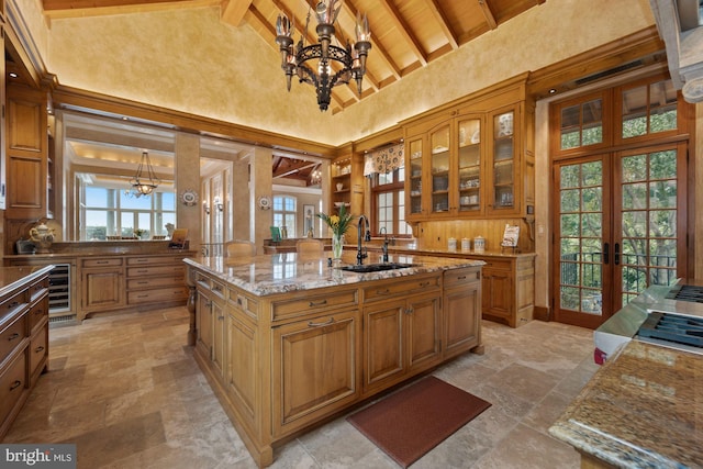 kitchen with french doors, light stone counters, a center island with sink, high vaulted ceiling, and hanging light fixtures