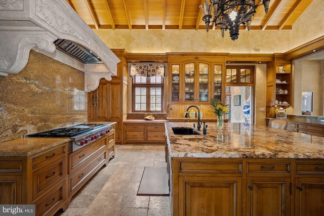 kitchen with light stone counters, sink, an island with sink, ventilation hood, and beam ceiling