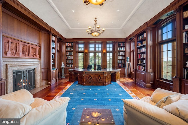 home office featuring hardwood / wood-style floors, built in features, an inviting chandelier, and a tray ceiling