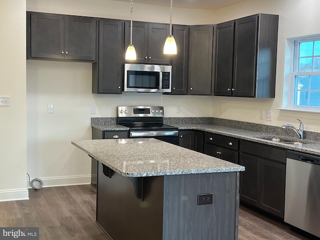 kitchen with stainless steel appliances, dark hardwood / wood-style floors, light stone countertops, hanging light fixtures, and sink