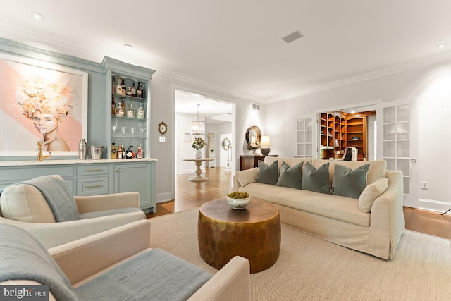 living room with a chandelier, french doors, crown molding, and light hardwood / wood-style flooring