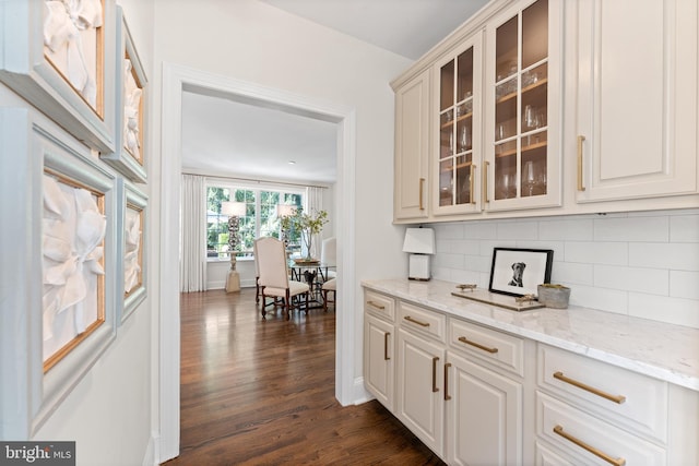 bar featuring light stone countertops, decorative backsplash, white cabinets, and dark wood-type flooring