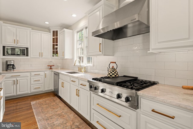 kitchen featuring hardwood / wood-style floors, wall chimney range hood, sink, white cabinetry, and stainless steel appliances