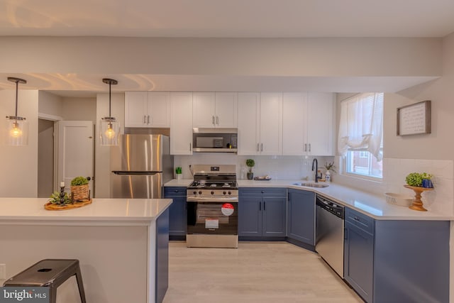 kitchen with stainless steel appliances, light hardwood / wood-style floors, white cabinetry, sink, and hanging light fixtures