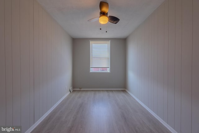 spare room featuring ceiling fan, wooden walls, and light wood-type flooring