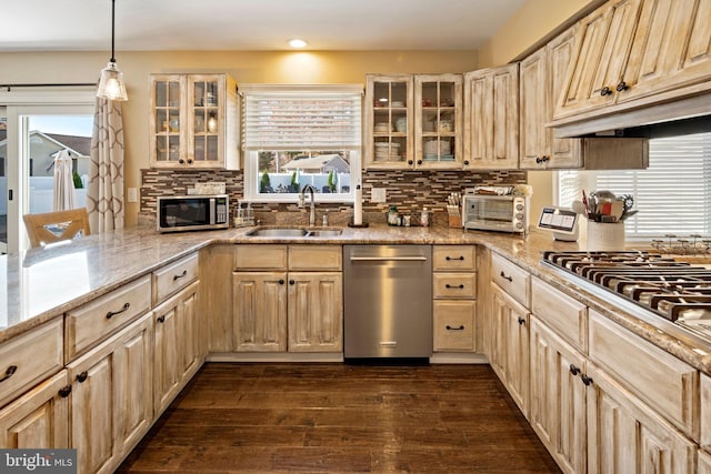 kitchen with stainless steel appliances, light brown cabinetry, hanging light fixtures, sink, and dark wood-type flooring