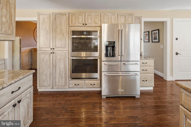 kitchen with light stone countertops, appliances with stainless steel finishes, light brown cabinetry, and dark hardwood / wood-style flooring