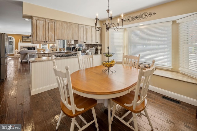 dining space with dark wood-type flooring, a tile fireplace, and a notable chandelier