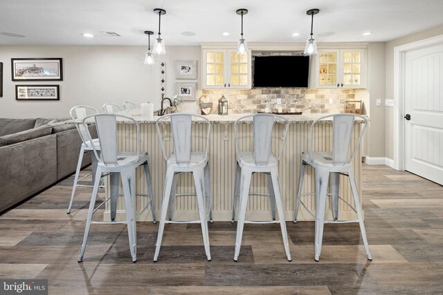 bar with tasteful backsplash, light stone countertops, decorative light fixtures, and light hardwood / wood-style flooring