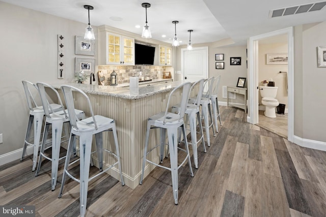 bar with backsplash, hanging light fixtures, wood-type flooring, and light stone countertops