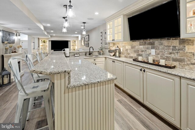 kitchen featuring light stone counters, a breakfast bar area, backsplash, light hardwood / wood-style flooring, and decorative light fixtures