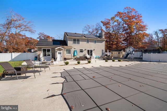 back of property featuring a patio, solar panels, a covered pool, and a storage unit