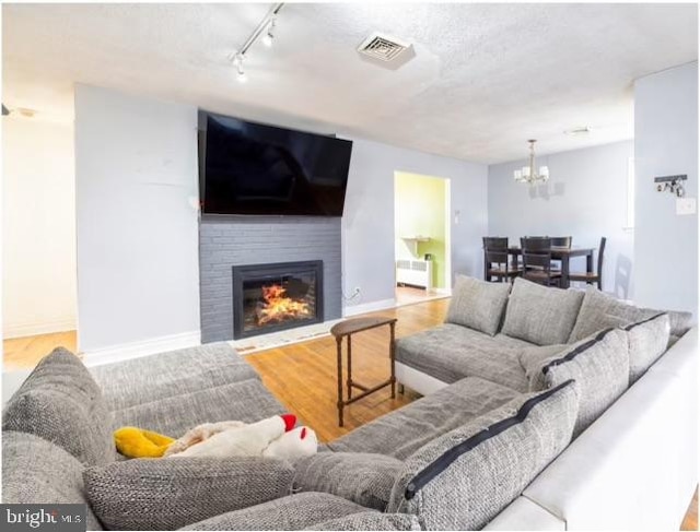 living room featuring radiator, wood-type flooring, a textured ceiling, a brick fireplace, and rail lighting