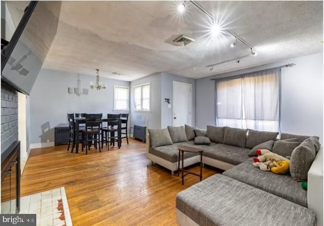 living room featuring track lighting, a notable chandelier, a textured ceiling, hardwood / wood-style flooring, and a fireplace