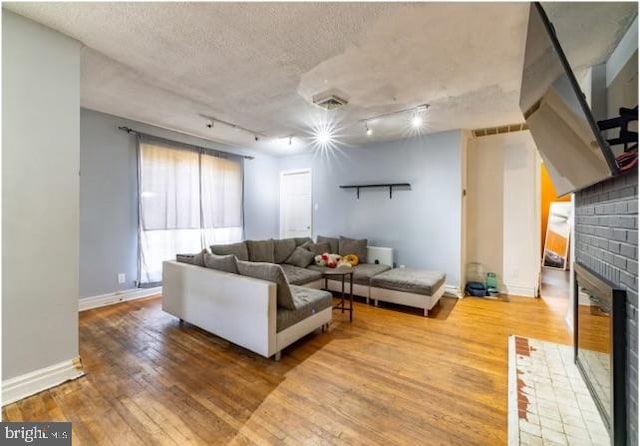 living room with a textured ceiling, a fireplace, track lighting, and wood-type flooring