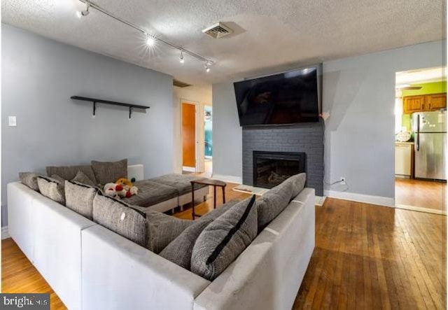 living room featuring a brick fireplace, rail lighting, wood-type flooring, and a textured ceiling