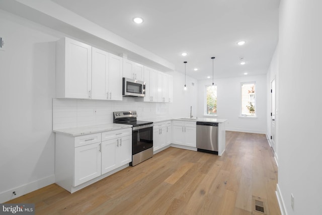 kitchen with kitchen peninsula, stainless steel appliances, tasteful backsplash, decorative light fixtures, and white cabinets