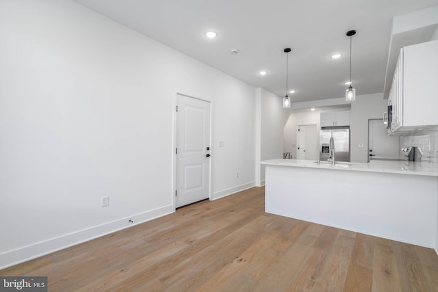 kitchen featuring kitchen peninsula, white cabinetry, hanging light fixtures, light wood-type flooring, and appliances with stainless steel finishes