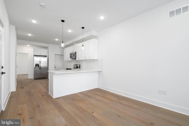 kitchen with white cabinets, stainless steel appliances, decorative backsplash, hanging light fixtures, and kitchen peninsula