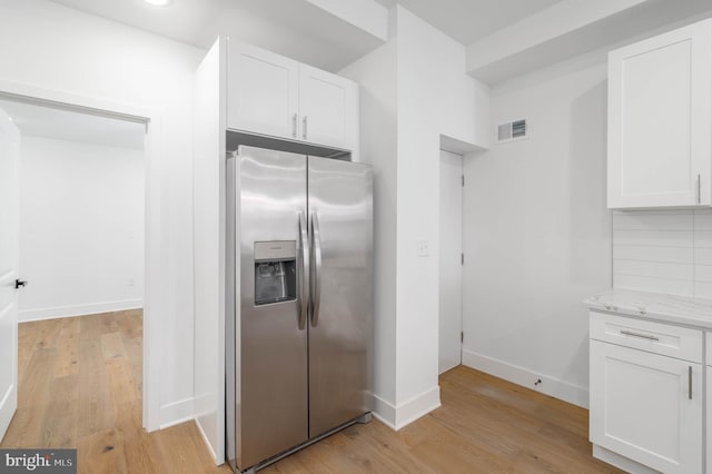 kitchen with backsplash, stainless steel refrigerator with ice dispenser, white cabinetry, light hardwood / wood-style flooring, and light stone counters