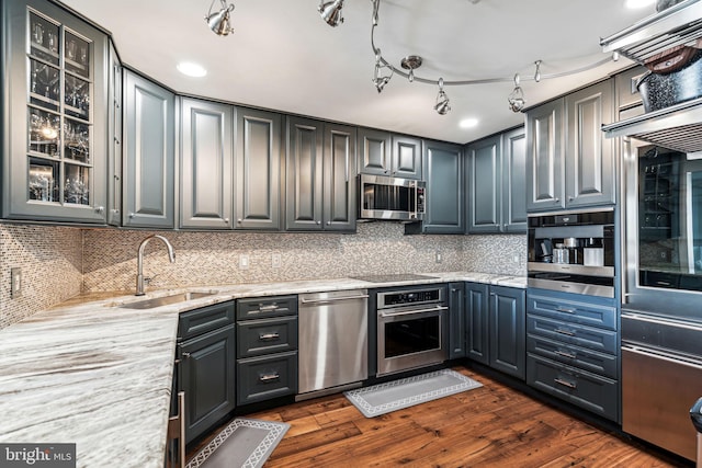 kitchen with dark wood-type flooring, sink, decorative backsplash, light stone countertops, and stainless steel appliances