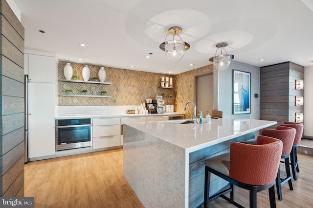 kitchen with stainless steel oven, sink, light hardwood / wood-style floors, decorative light fixtures, and white cabinets