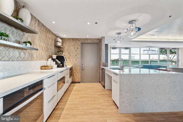 kitchen with light hardwood / wood-style flooring, white cabinetry, hanging light fixtures, and sink