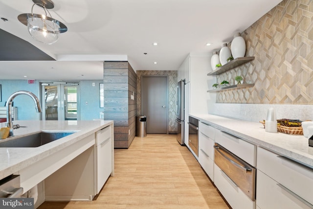 kitchen with sink, light hardwood / wood-style flooring, light stone countertops, white cabinetry, and stainless steel appliances