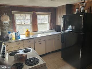 kitchen featuring light tile patterned flooring, black refrigerator, stove, and white cabinetry