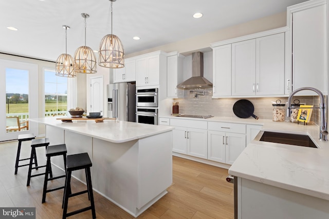 kitchen featuring white cabinetry, appliances with stainless steel finishes, pendant lighting, sink, and wall chimney exhaust hood